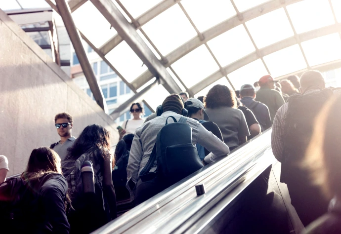 People riding an escalator towards bright sunlight.